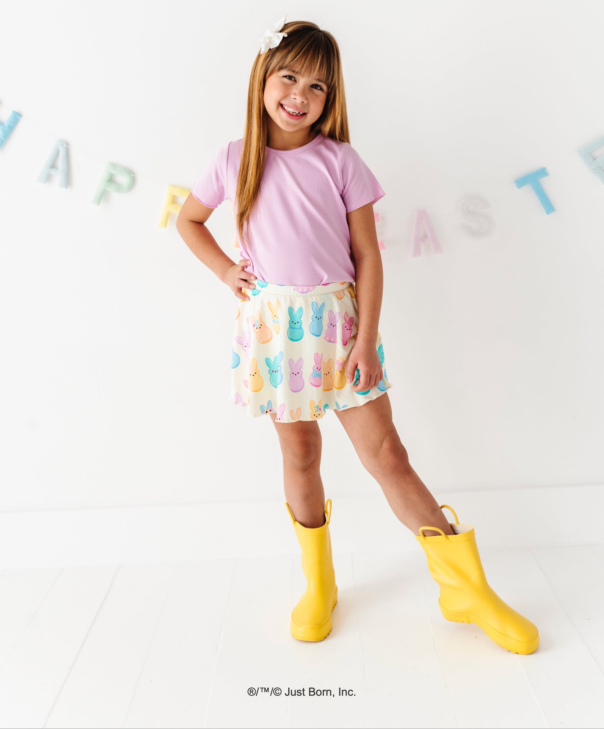 Child wearing a pink shirt, colorful PEEPS® skirt, and yellow rain boots on a white background with colorful letters.