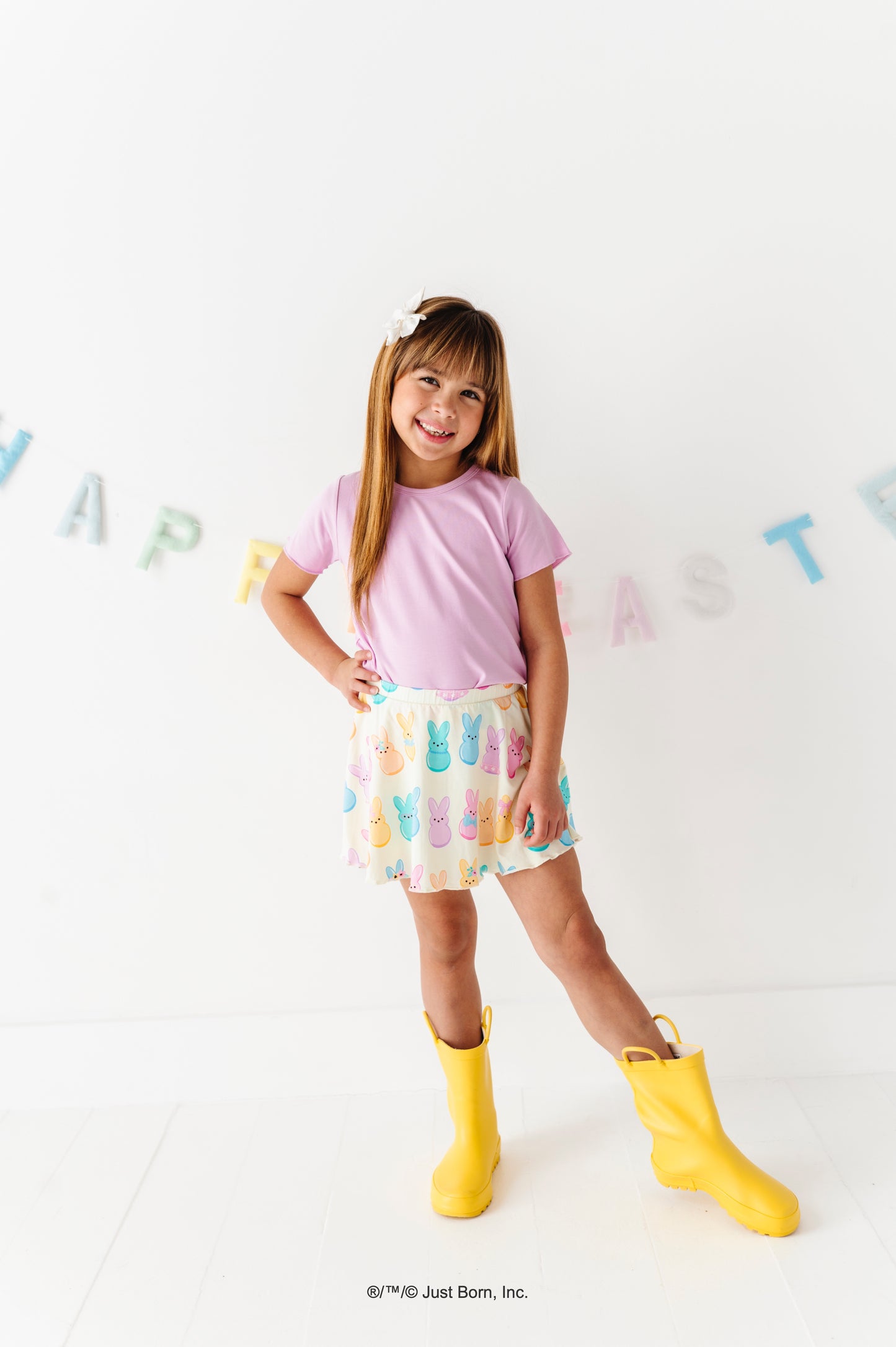 Child wearing a bamboo blend lavender shirt, colorful PEEPS® skirt, and yellow rain boots on a white background with colorful letters.
