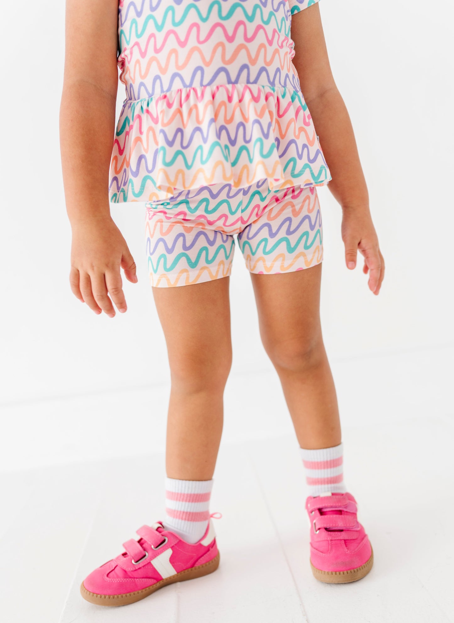Child wearing a colorful striped outfit with pink shoes and socks on a white background