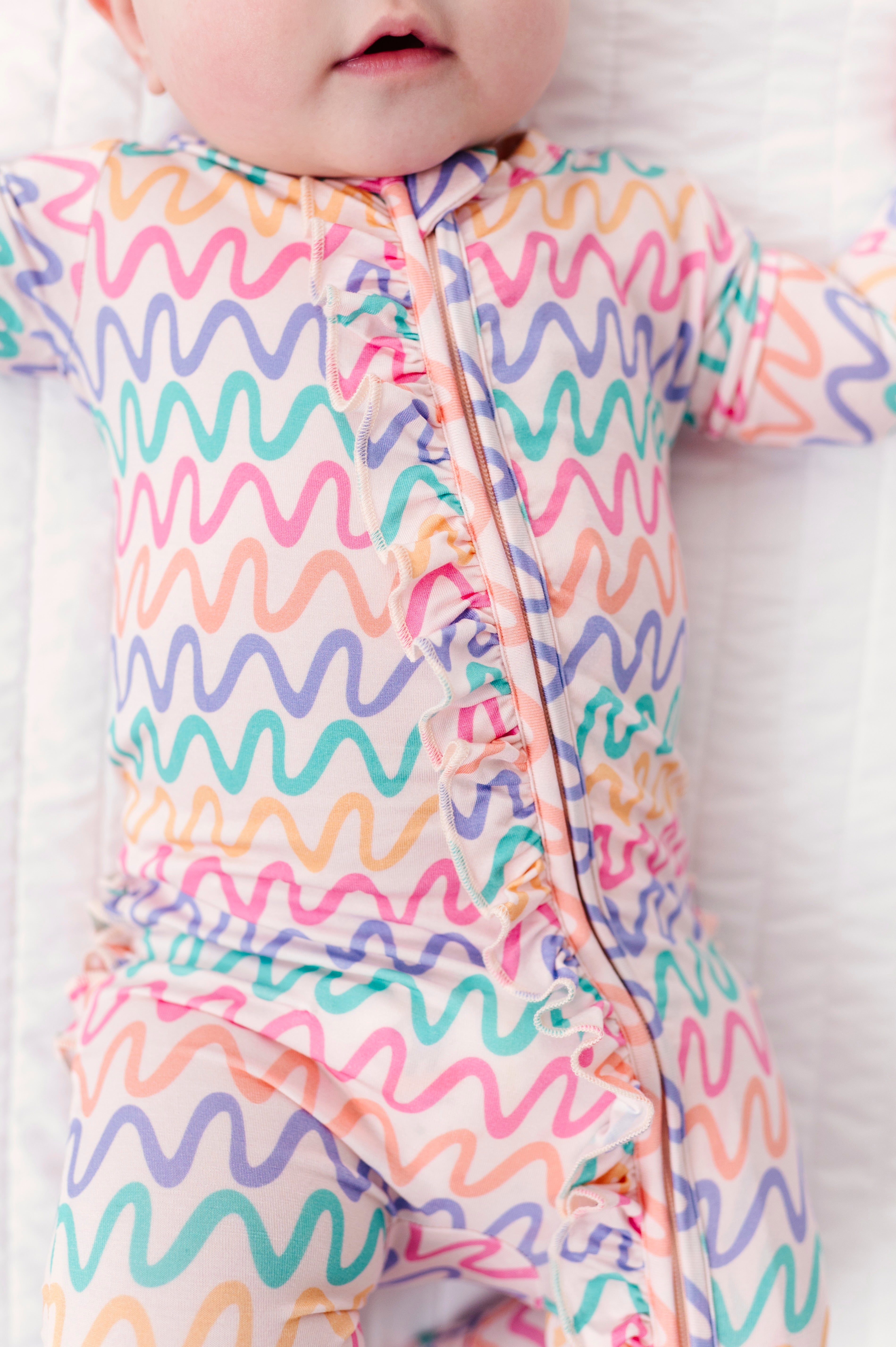 Baby wearing a colorful wavy patterned bamboo convertible romper on a white background