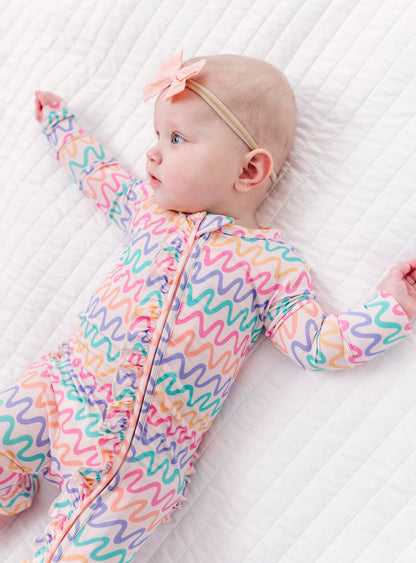 Baby wearing a colorful wavy patterned bamboo zip romper on a white textured surface