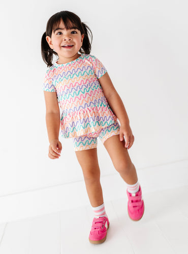 Little girl wearing a colorful squiggly pattern bamboo/cotton peplum top and coordinating biker shorts on a white background