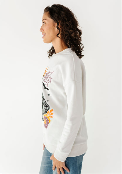 A woman in profile wearing a white crewneck sweatshirt with a colorful spiderweb and spider graphic on the front, paired with blue jeans, against a plain white background.
