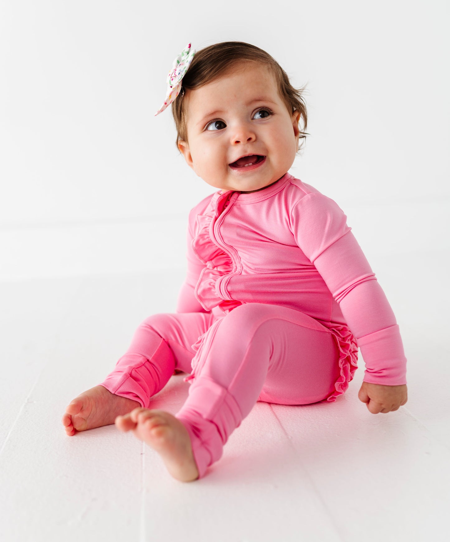Baby in a pink bamboo zip romper sitting on a white background