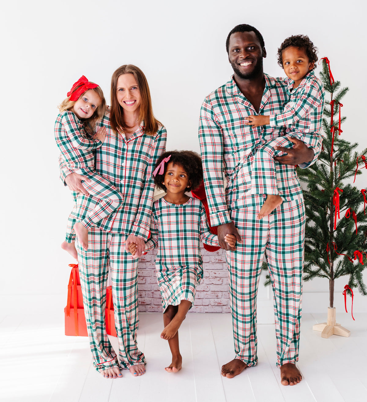 Mom, dad, and three children wearing matching classic Christmas plaid bamboo pajamas and standing in front of a Christmas tree