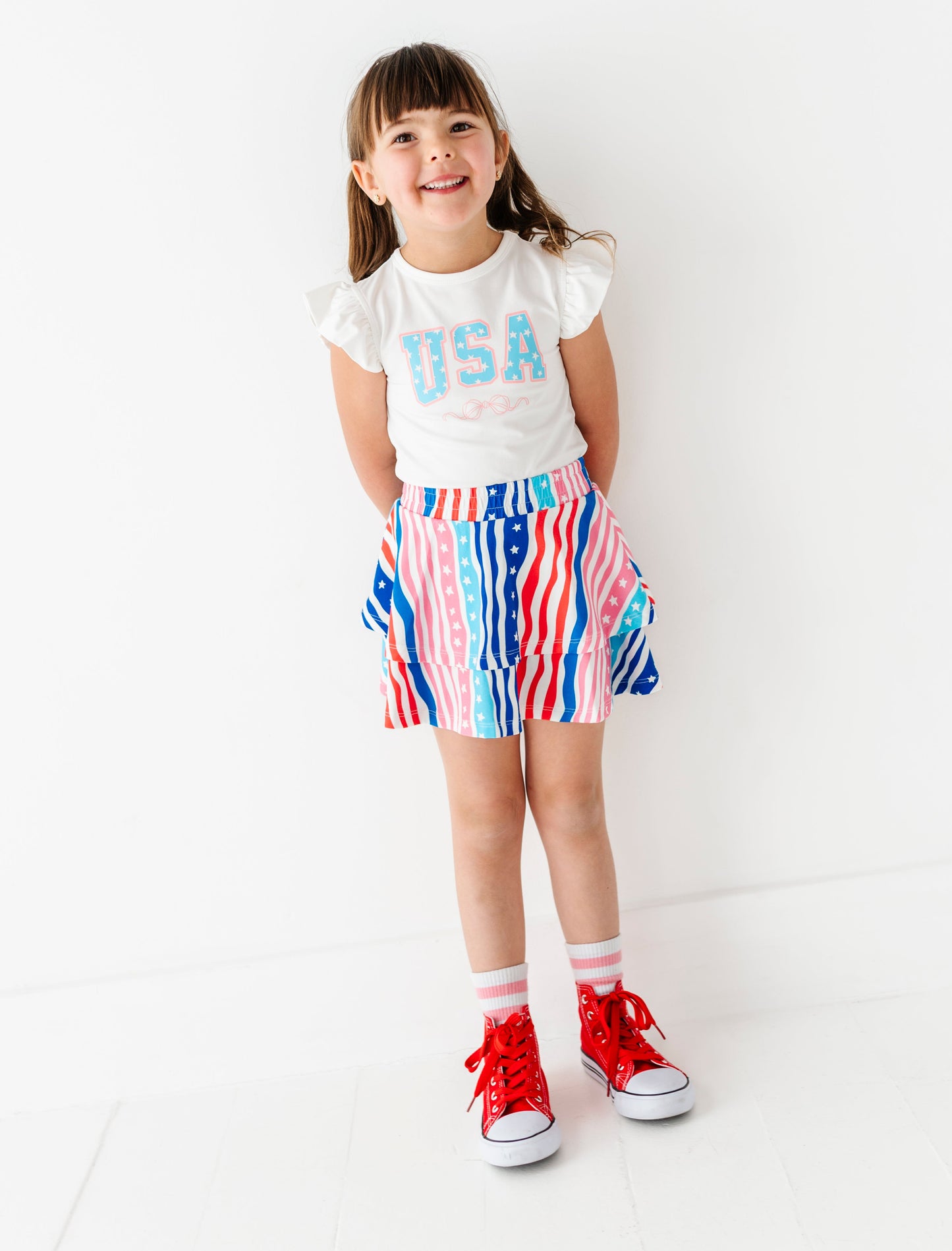 Child wearing a white t-shirt with 'USA' text and a colorful striped skirt on a white background