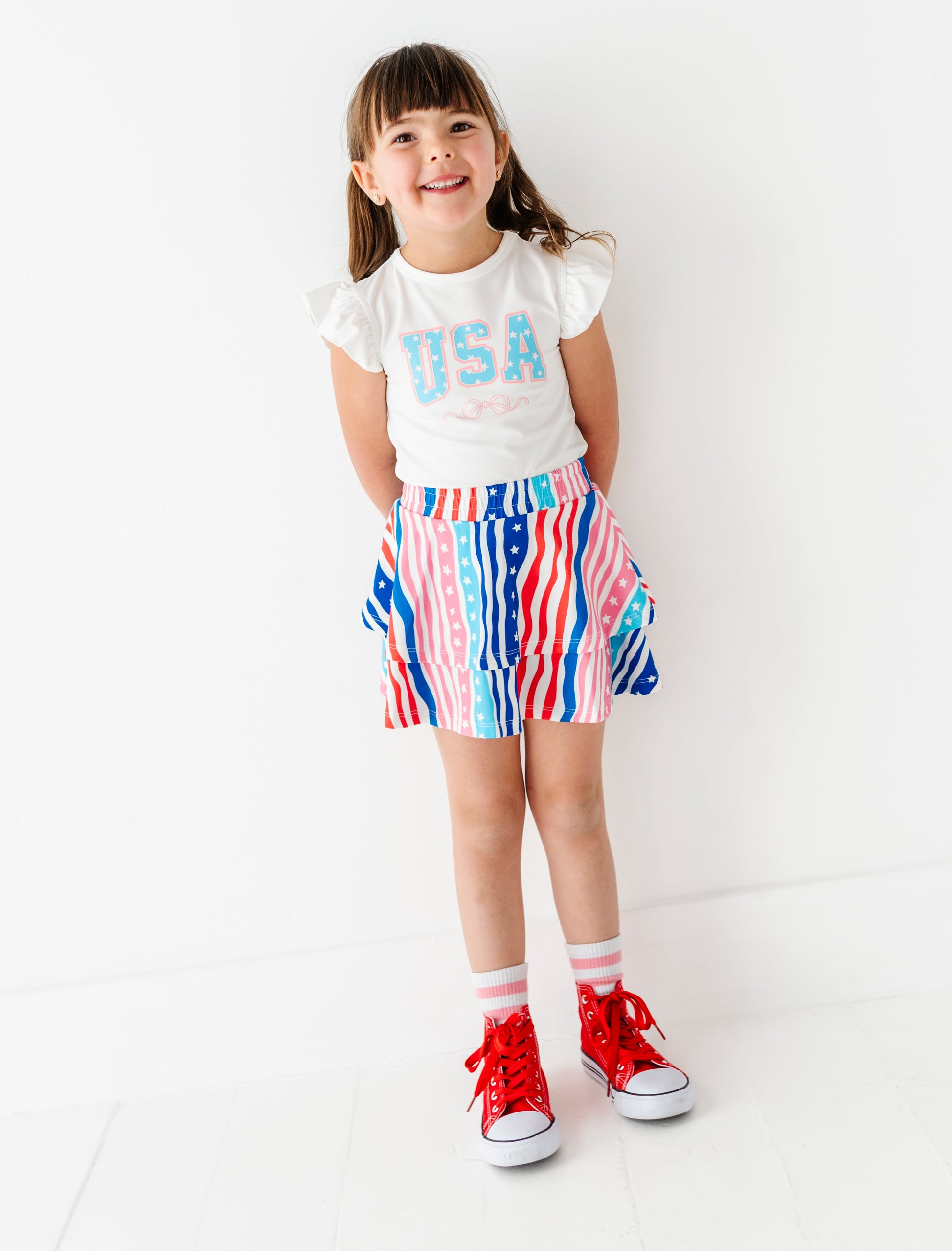 Child wearing a white t-shirt with 'USA' text and a colorful striped skirt on a white background