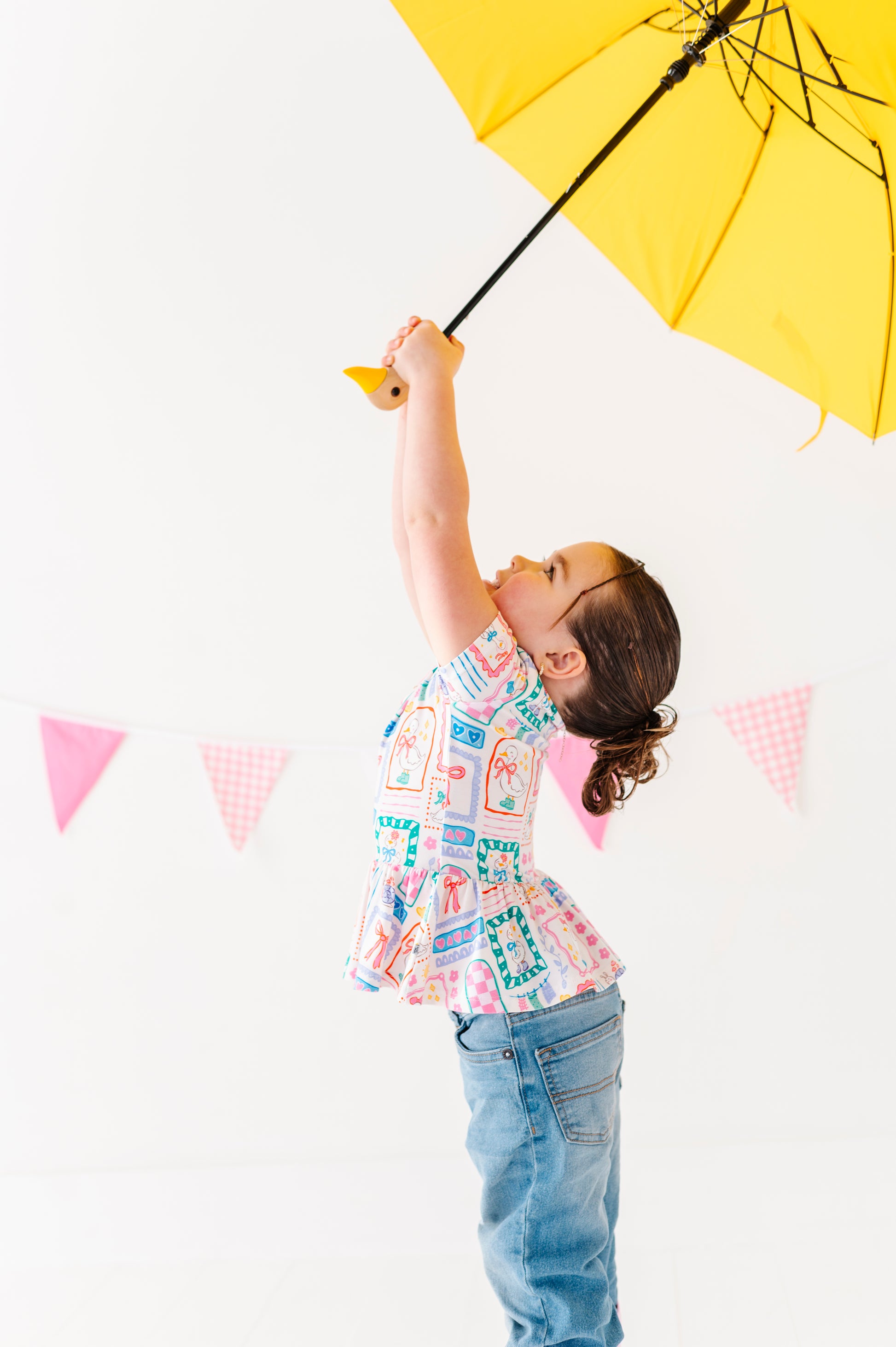 Child holding a yellow umbrella against a white background with colorful flags.