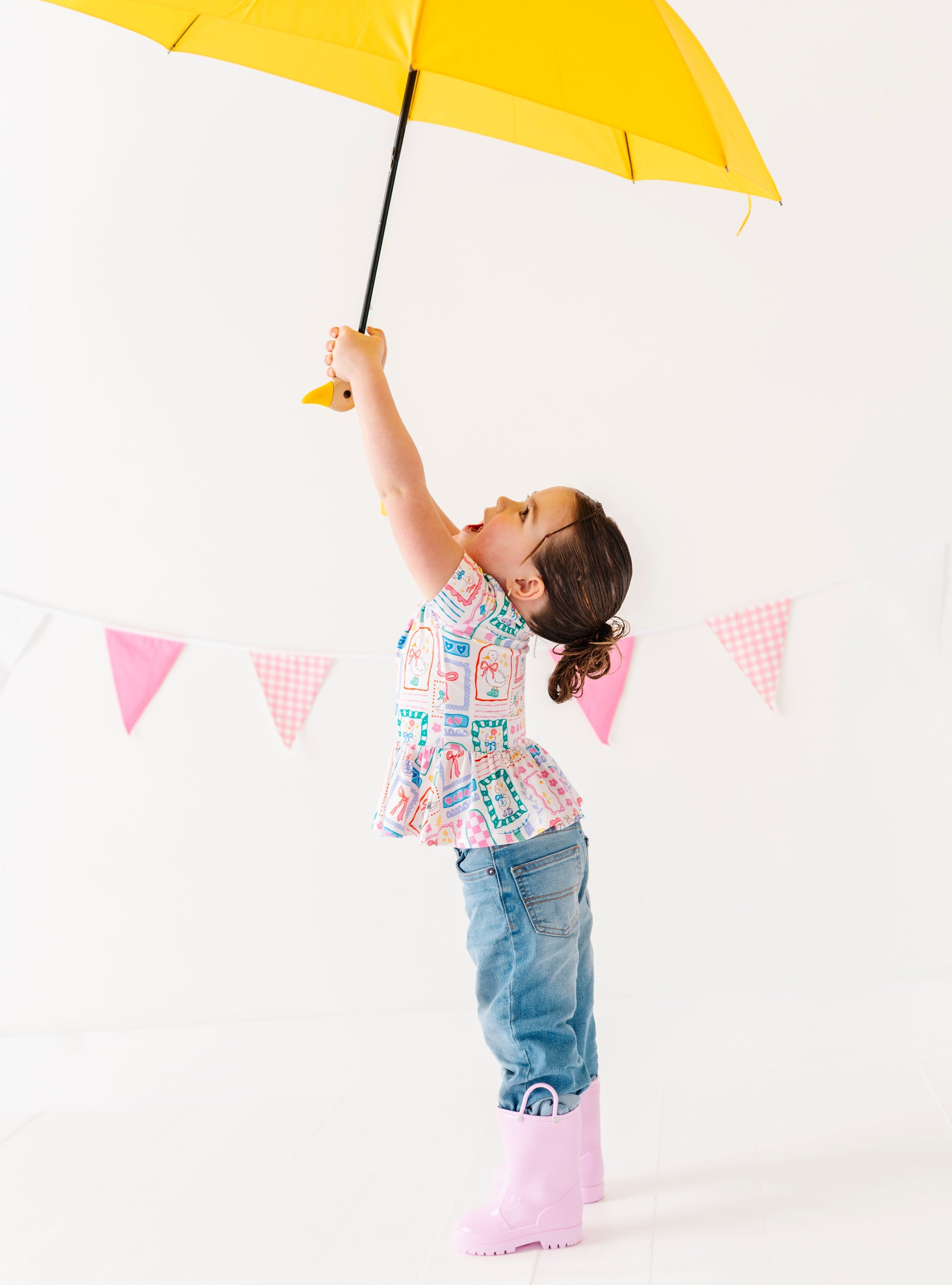 Child holding a yellow umbrella against a white background with pink flags.