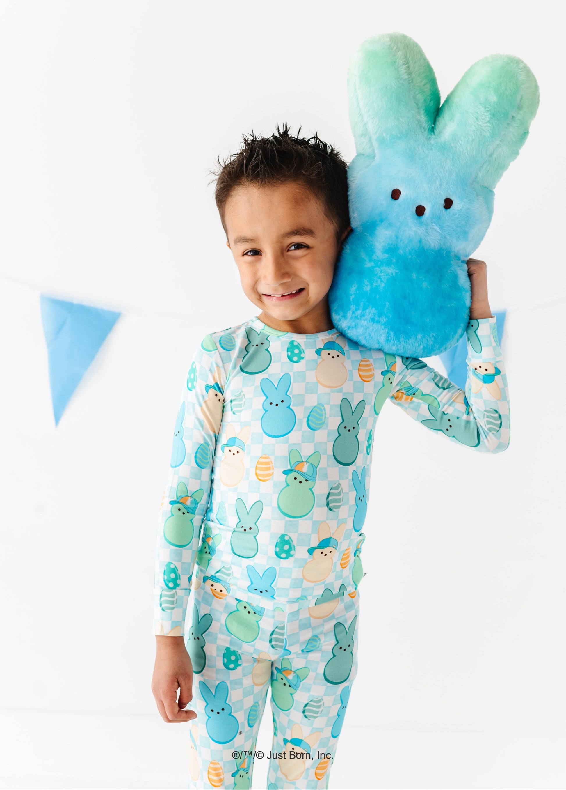 Child wearing a pajama with PEEPS® design, holding a blue plush toy, on a white background.
