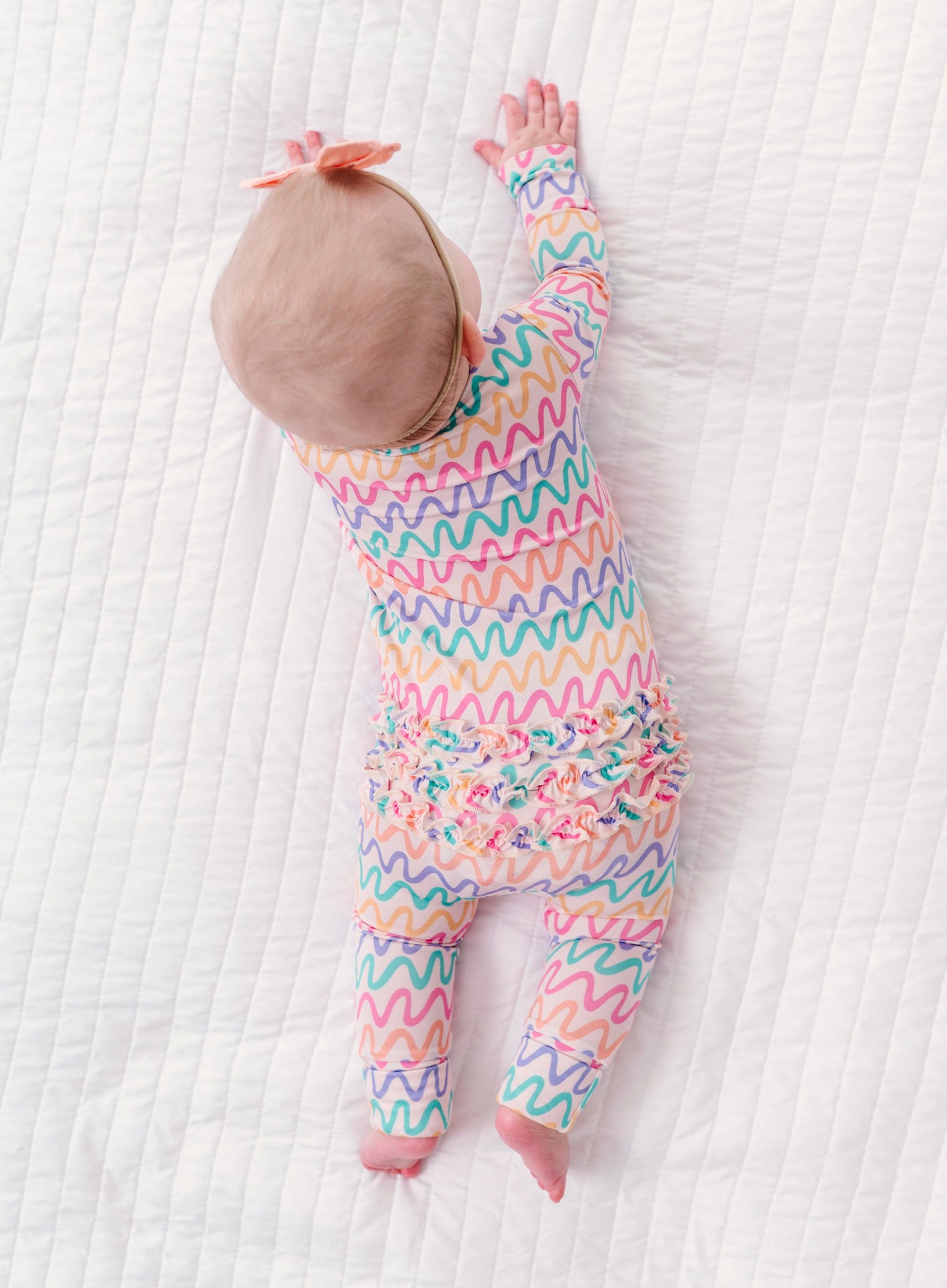 Baby in a colorful wavy patterned bamboo convertible romper on a white textured surface