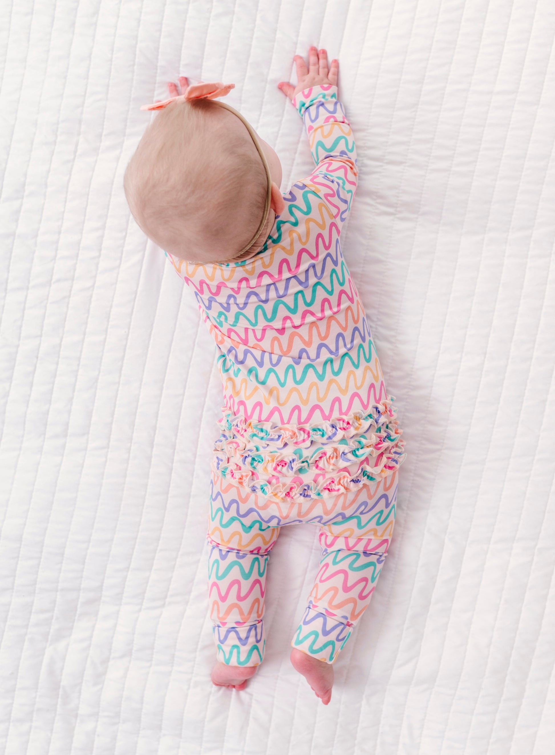 Baby in a colorful wavy patterned bamboo convertible romper on a white textured surface