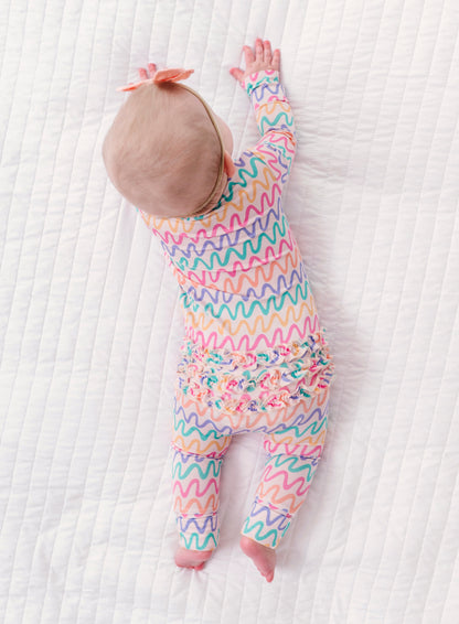 Baby in a colorful wavy patterned bamboo convertible romper on a white textured surface