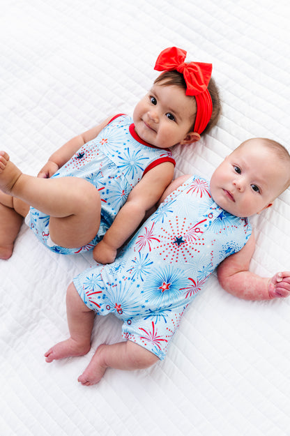 Two babies wearing coordinating 4th of July bamboo outfits with a red bow on a white blanket