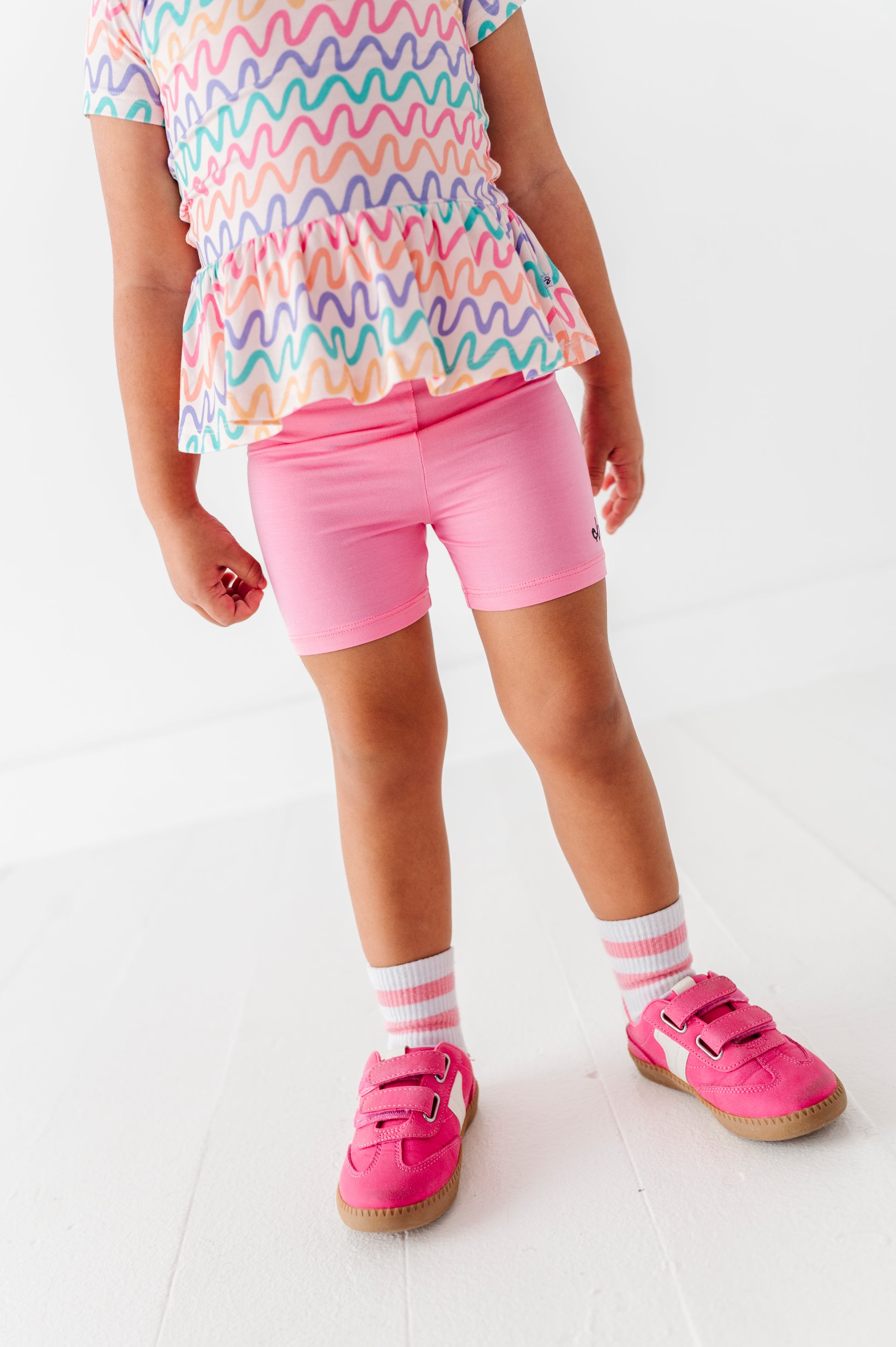 Child wearing a colorful bamboo/cotton peplum top and pink bamboo shorts on a white background