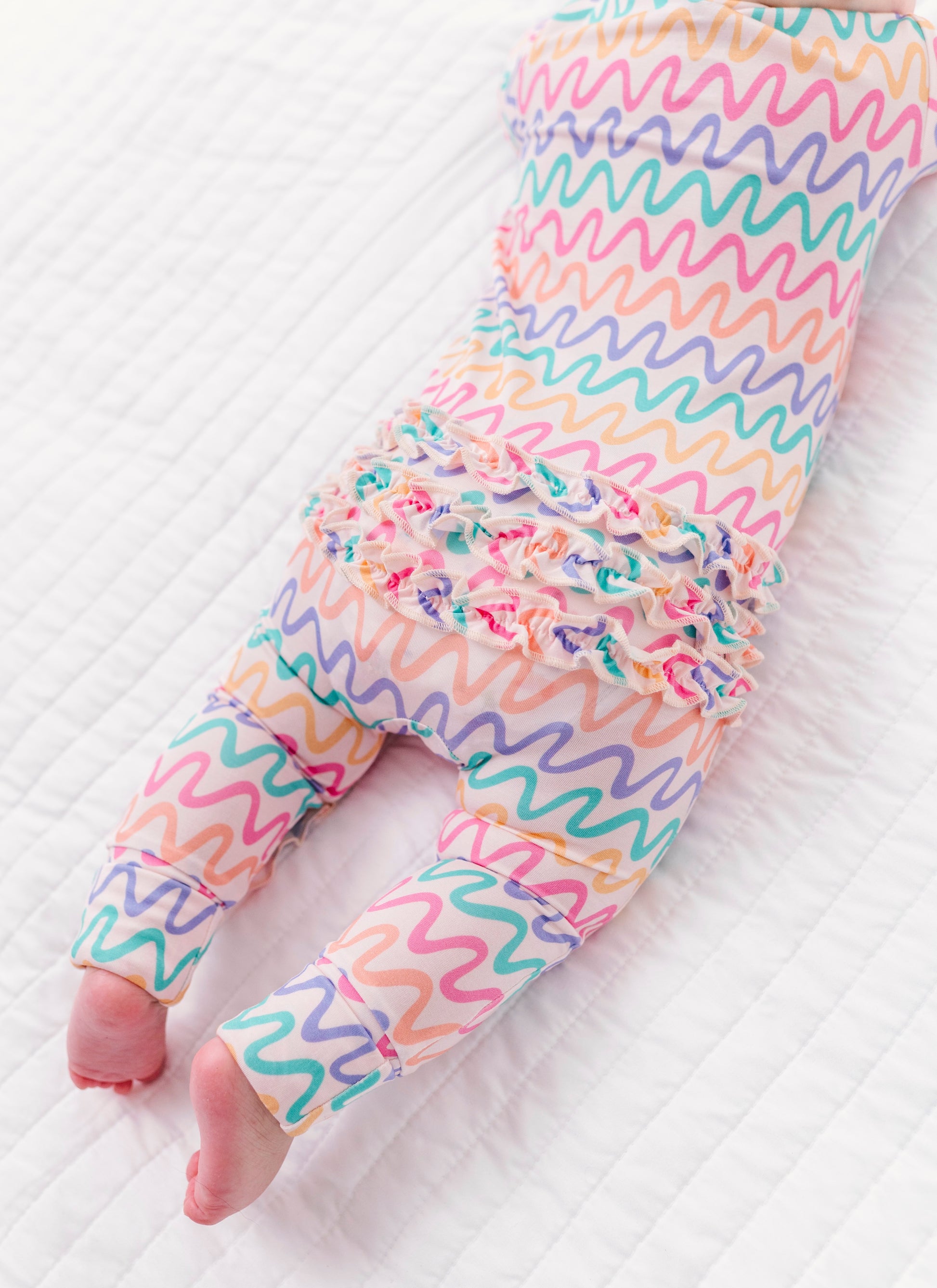 Colorful wavy-patterned bamboo pajamas with ruffles on a baby 