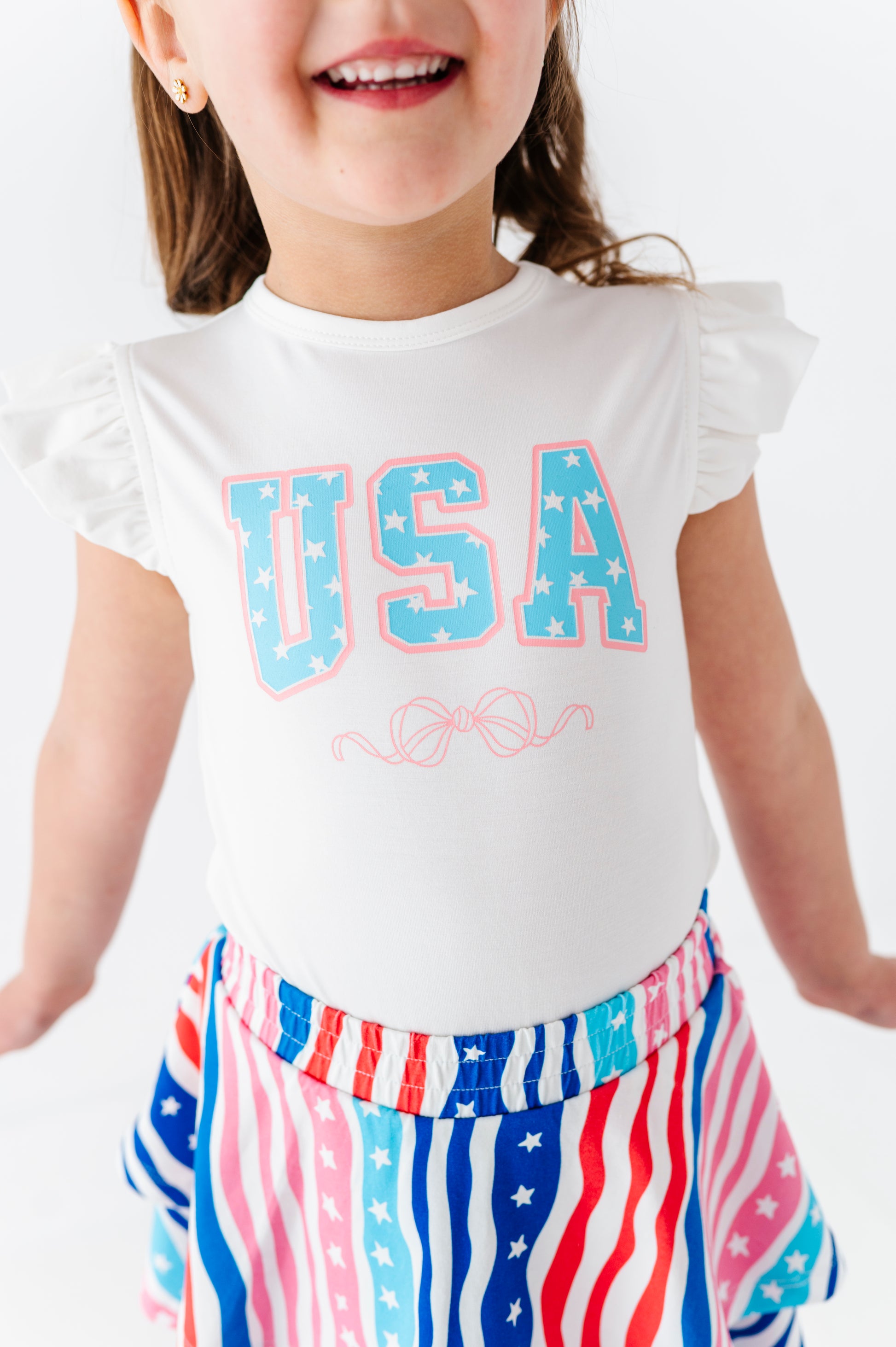 Child wearing a white 'USA' bamboo-cotton t-shirt with a patriotic skort on a plain background