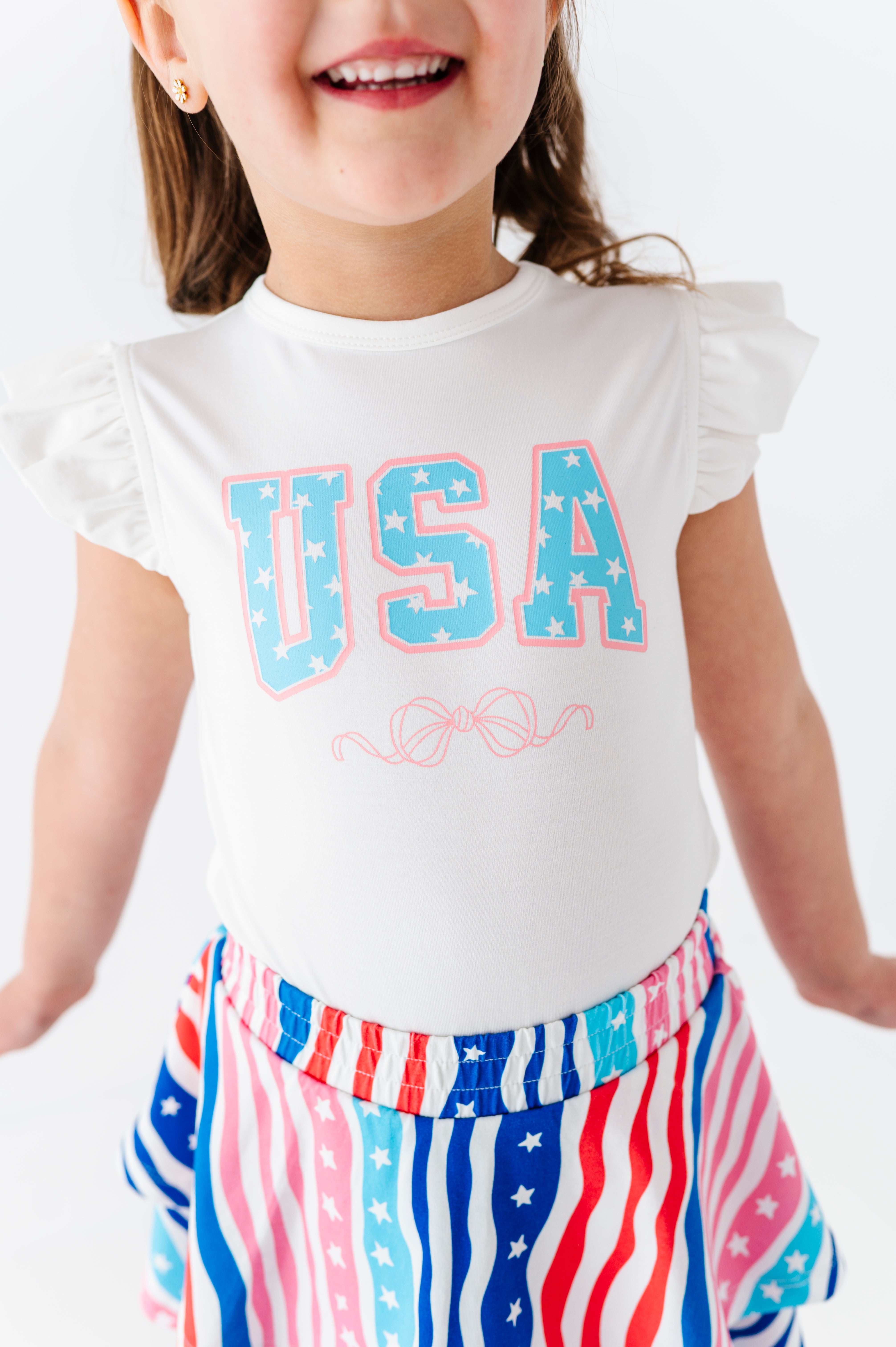 Child wearing a white 'USA' bamboo-cotton t-shirt with a patriotic skort on a plain background