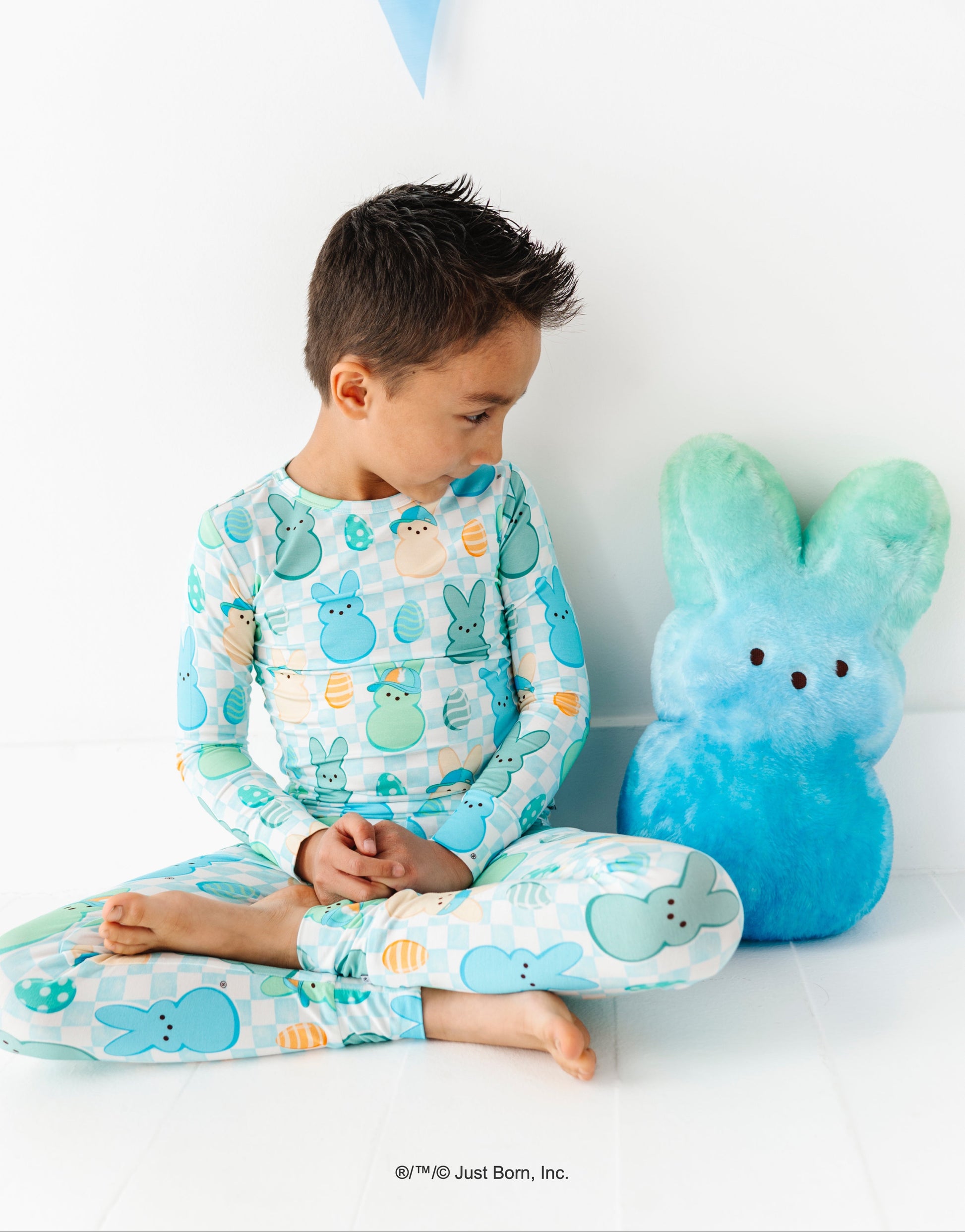 Child wearing Peep-themed pajamas sitting next to a blue plush PEEPS® toy with a white background