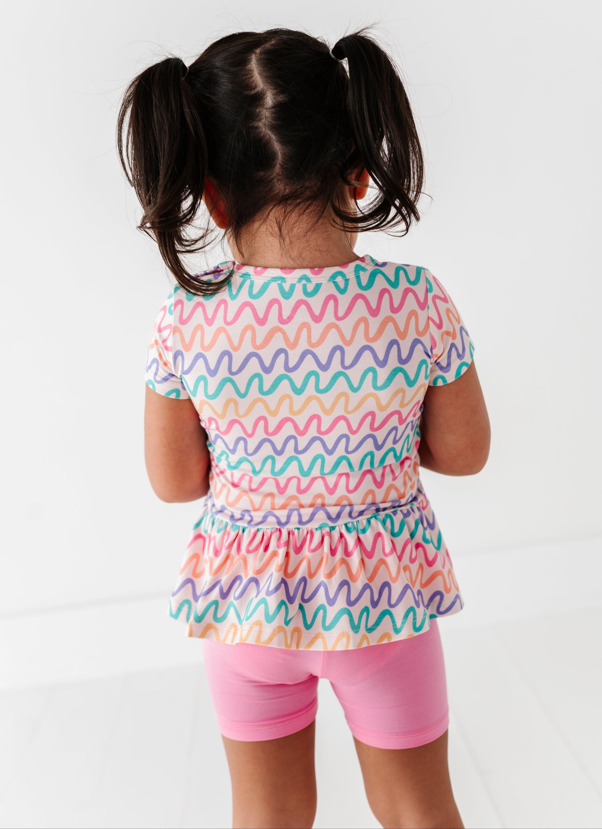 Child wearing a colorful wavy patterned bamboo/cotton shirt and pink bamboo biker shorts on a white background