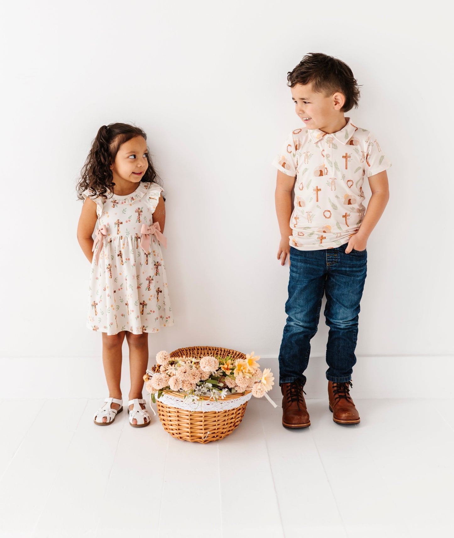 Two children standing next to a basket of flowers on a white background