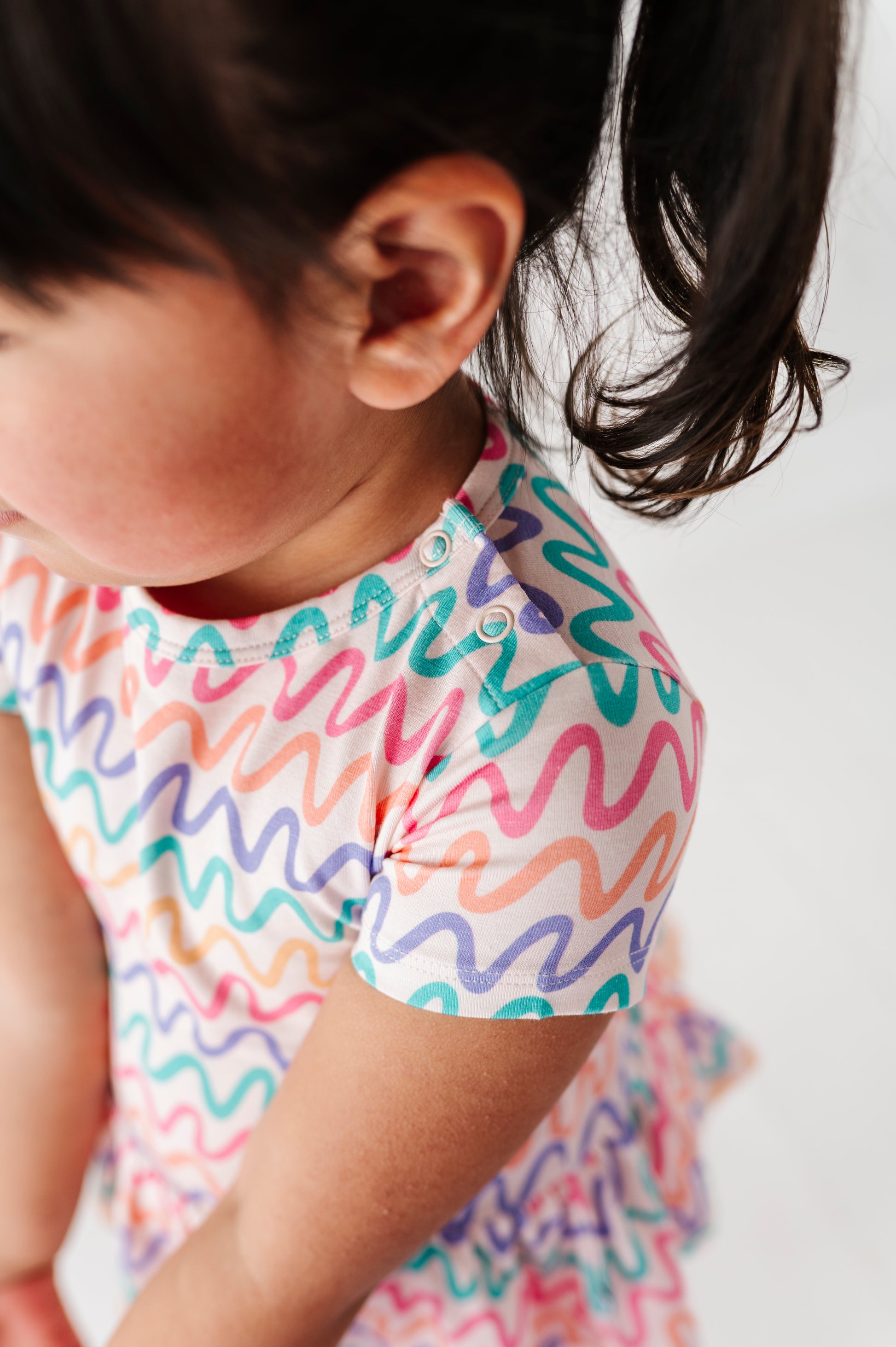 Little girl wearing a colorful patterned bamboo/cotton shirt on a plain background