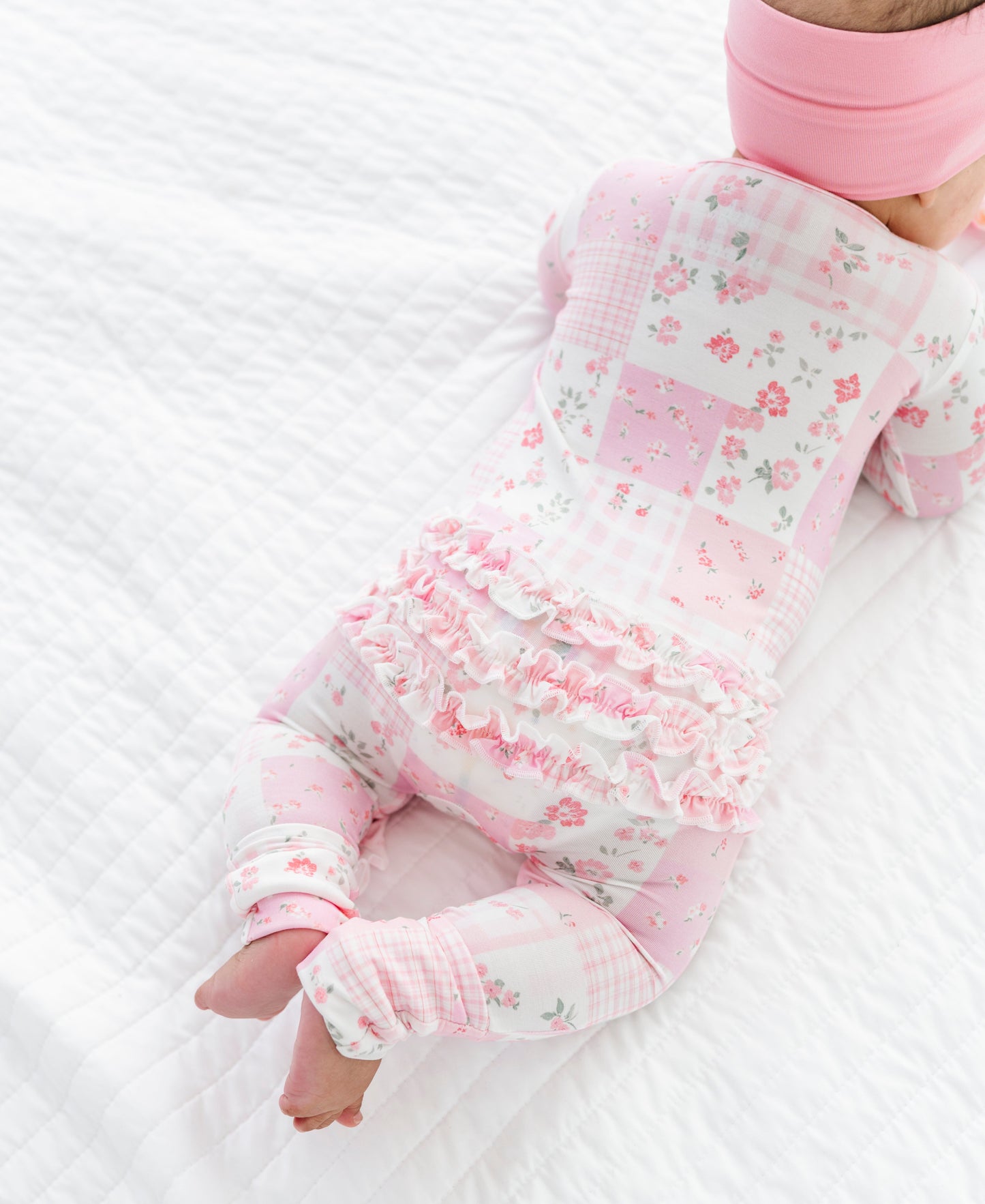 Baby in a floral bamboo zip romper and pink headband lying on a white textured surface