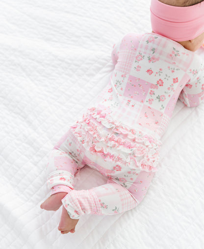 Baby in a floral bamboo zip romper and pink headband lying on a white textured surface