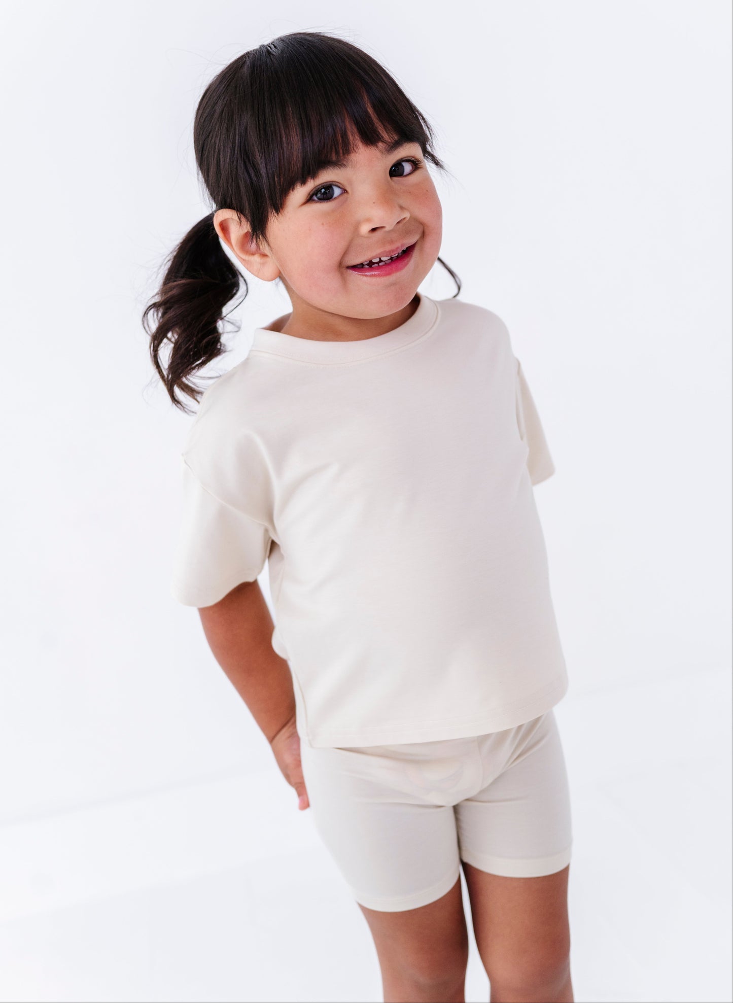 Young girl wearing an ivory t-shirt and ivory bamboo biker shorts on a white background