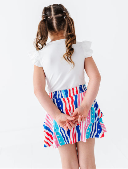 Child wearing a white top and colorful American flag skirt on a white background
