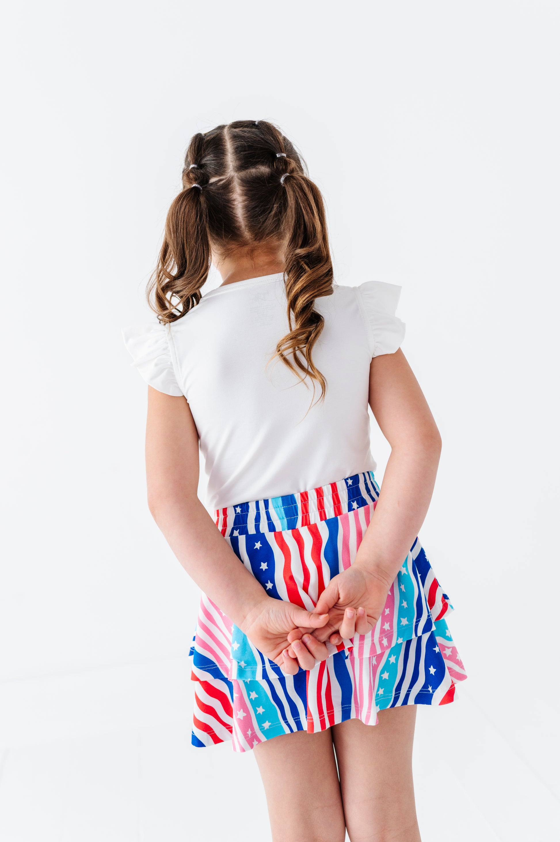 Child wearing a white bamboo-cotton top and colorful American flag skort on a white background