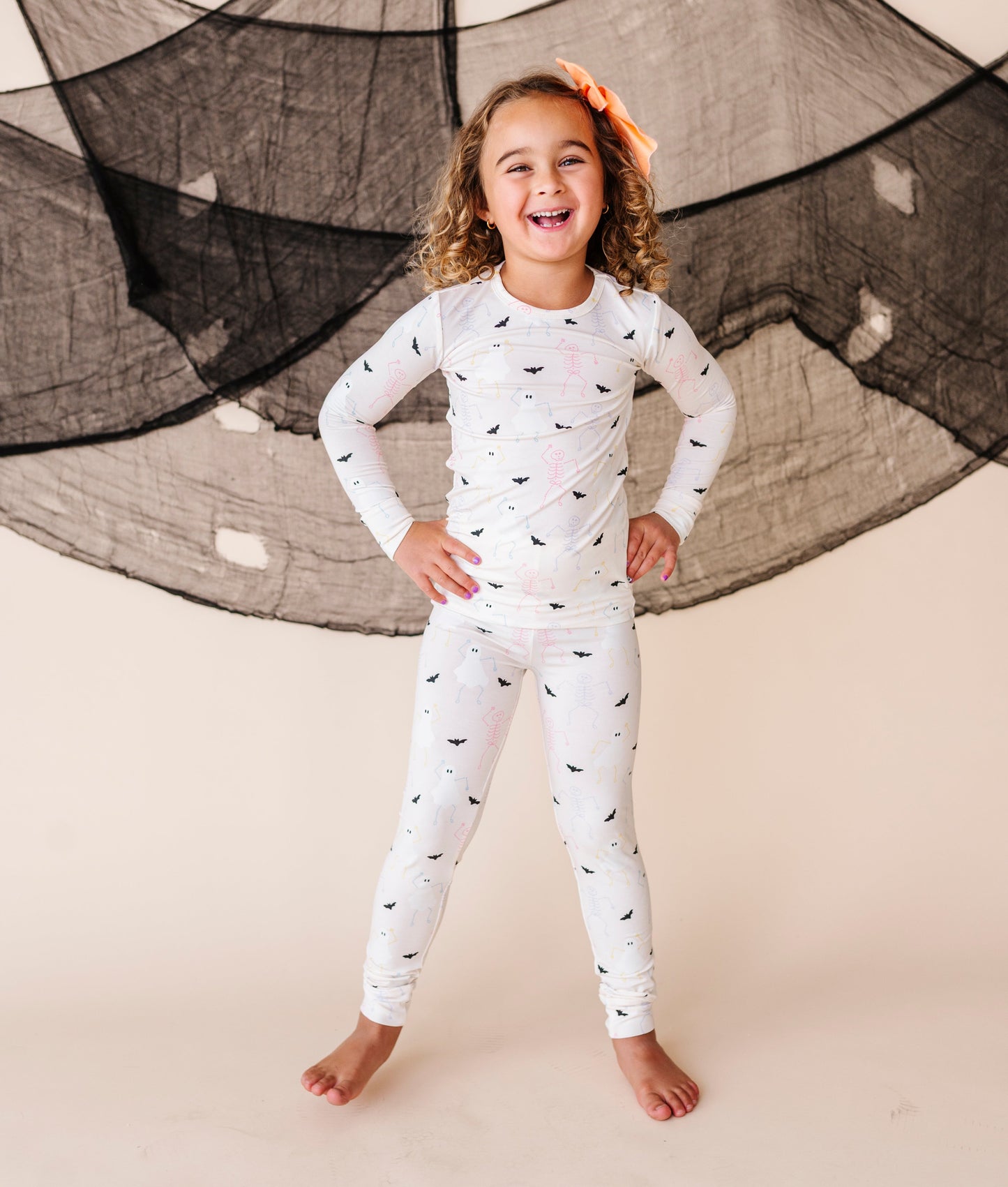 Child wearing a cream pajama set with Halloween  patterns against a neutral background