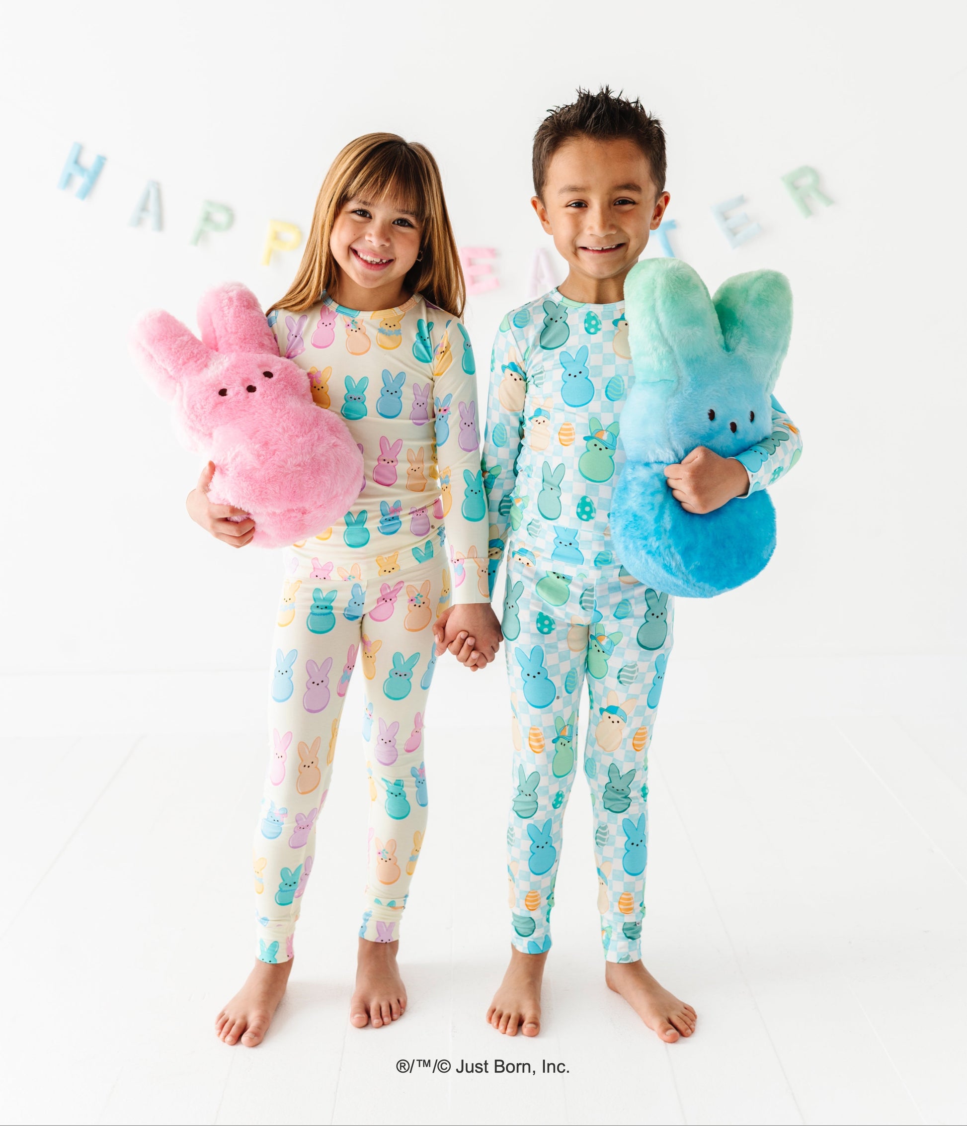 Two children wearing colorful pajamas holding stuffed animals with a 'Happy Easter' banner in the background.