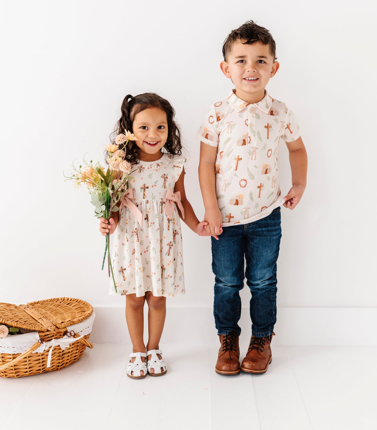 Two children, a girl and a boy, standing together on a white background with a basket and flowers.