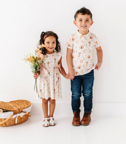Two children, a girl and a boy, standing together on a white background with a basket and flowers.