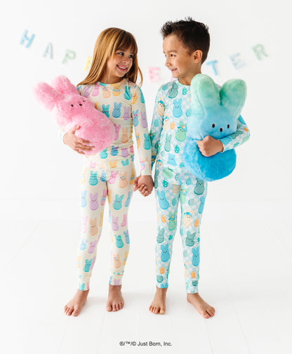 Two children in matching pajamas holding colorful stuffed PEEPS® toys with a 'Happy Easter' banner in the background.