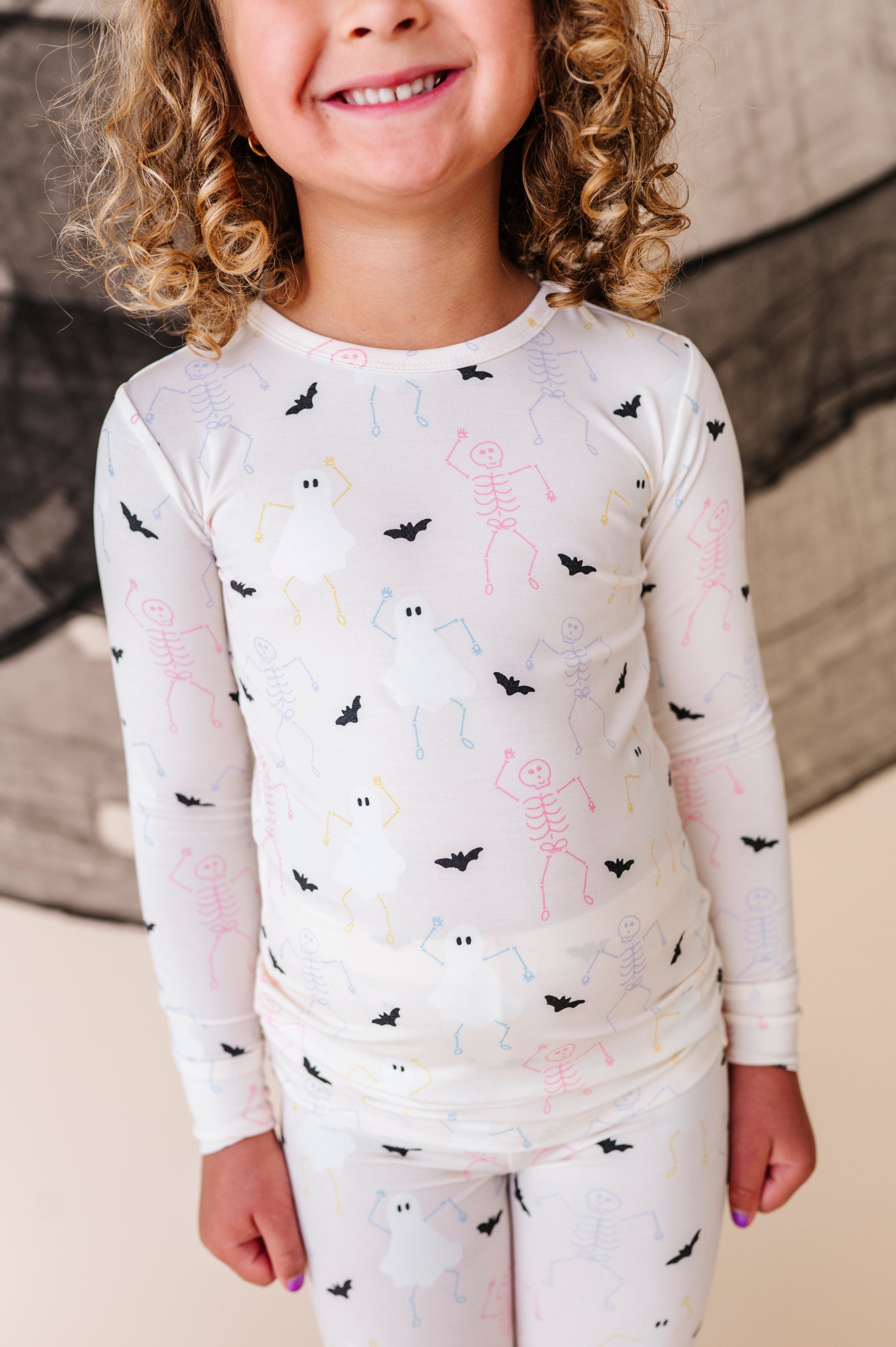 Child wearing a cream long-sleeve pajamas set with halloween and bat patterns in a studio setting
