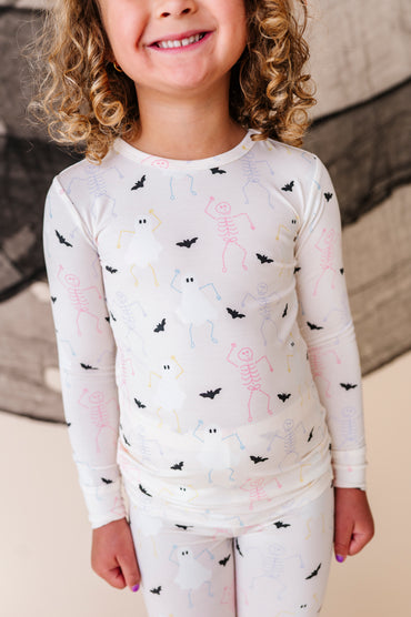 Child wearing a cream long-sleeve pajamas set with halloween and bat patterns in a studio setting