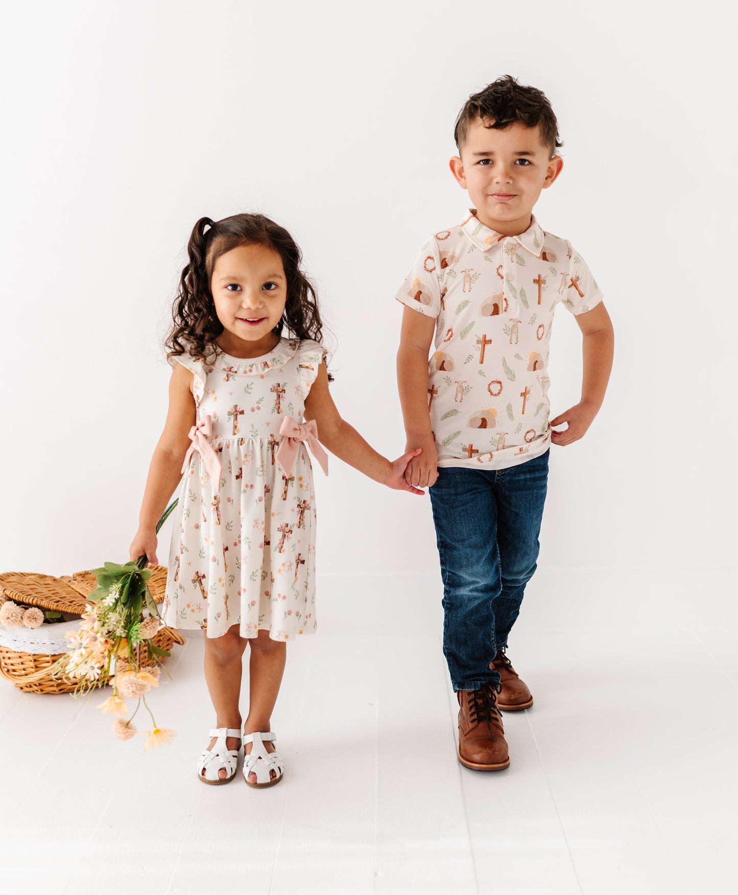 Two children, a girl and a boy, standing together on a white background. They're wearing traditional Easter-themed outfits made for Easter morning at church. 