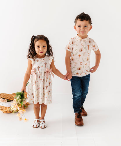 Two children, a girl and a boy, standing together on a white background. They're wearing traditional Easter-themed outfits made for Easter morning at church. 