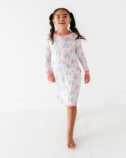 Young girl wearing a long sleeved lounging gown with watercolor rainbow pattern on a white background