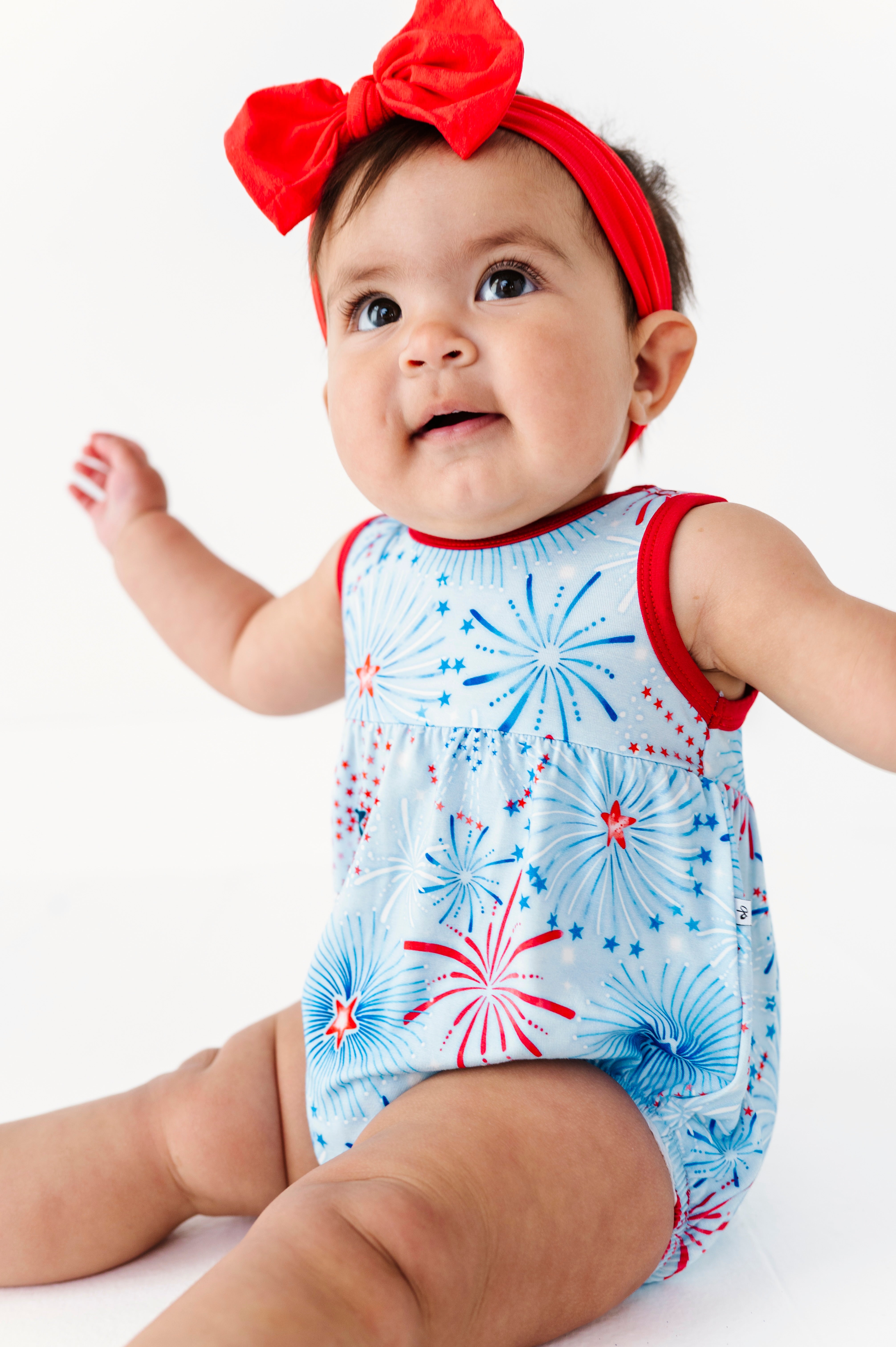 Baby wearing a red, white, and blue bamboo bubble romper with a bow headband on a white background