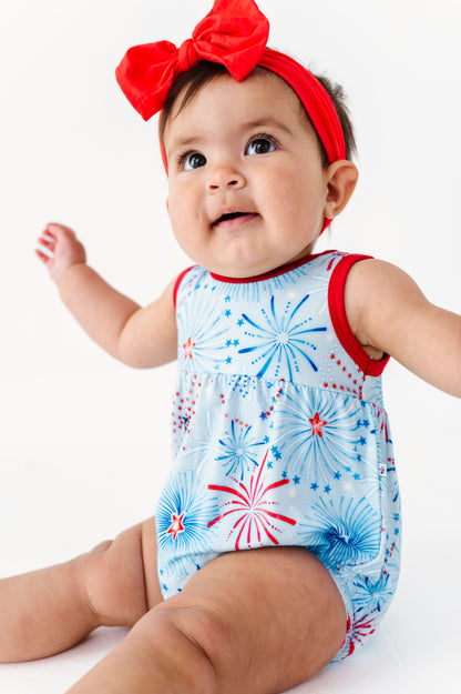 Baby wearing a red, white, and blue bamboo bubble romper with a bow headband on a white background