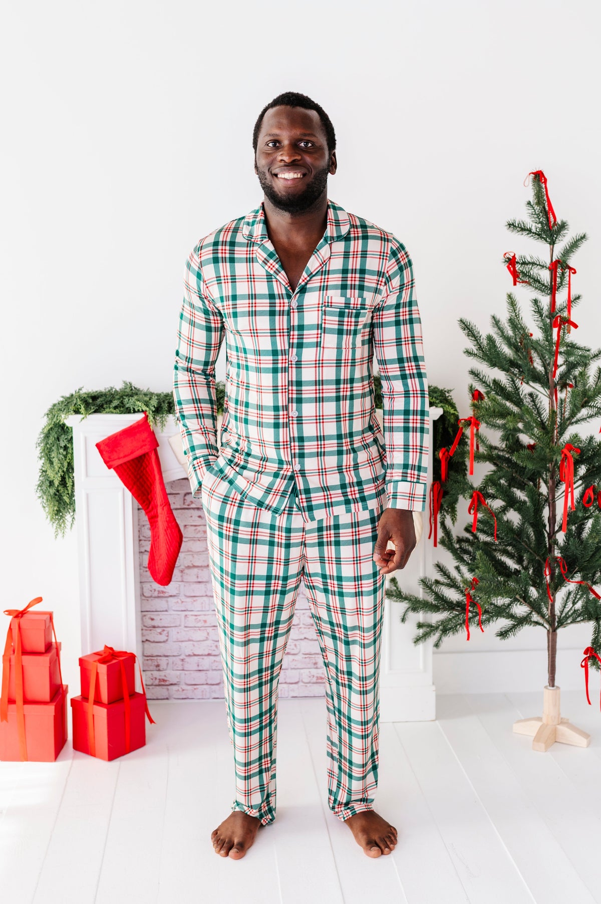 A man wearing a classic Christmas plaid lounge set and standing in front of a Christmas tree
