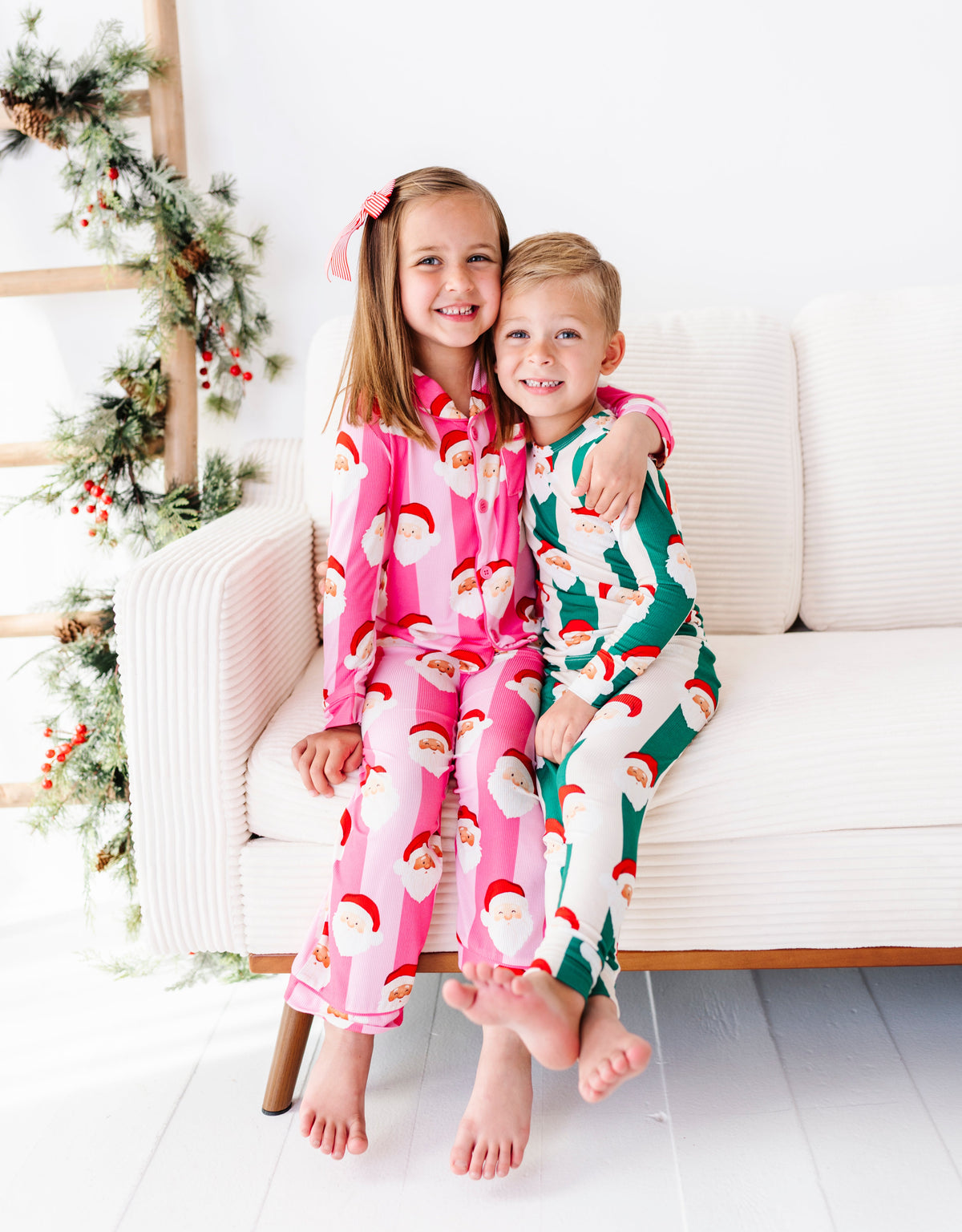 A little boy and his sister wearing coordinating stripe bamboo pajamas featuring various Santa faces all over the pajamas