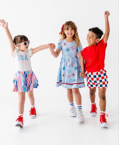 Three children in colorful 4th of July outfits standing together with arms raised on a white background