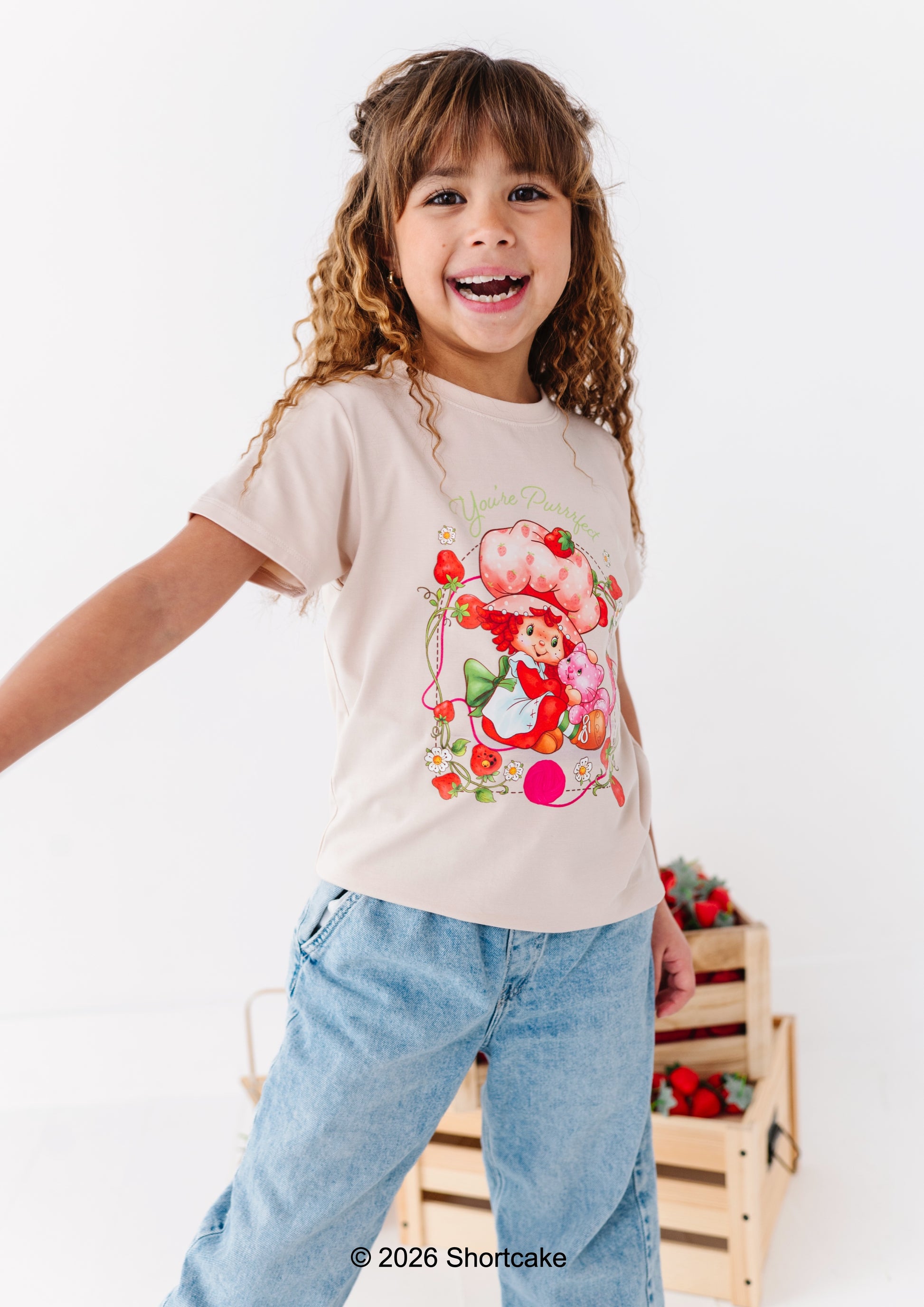 Child wearing an officially licensed Strawberry Shortcake™ t-shirt, standing next to a wooden crate with berries.