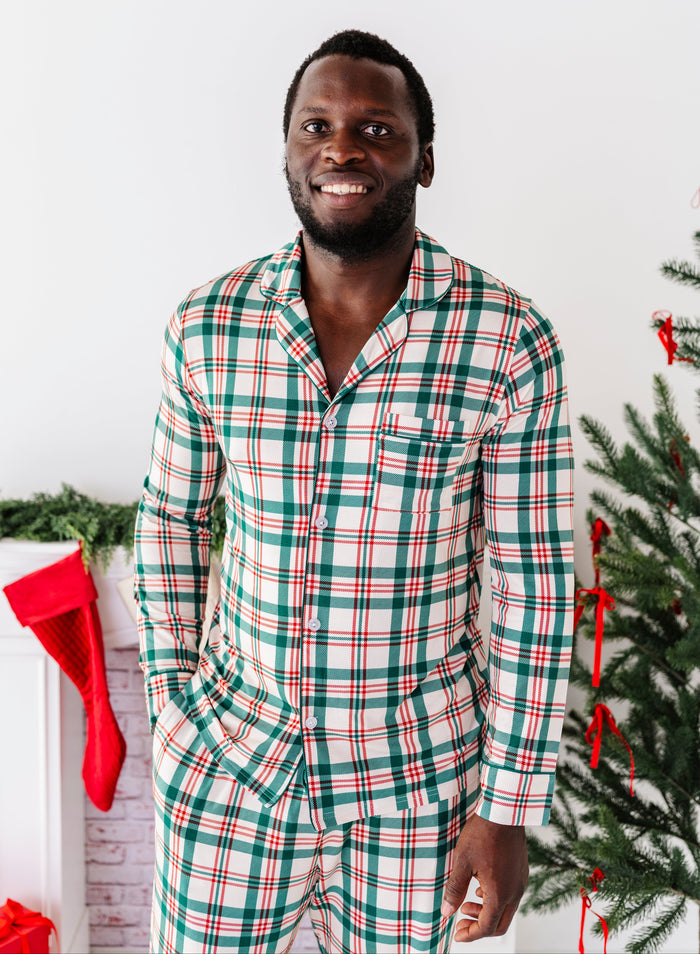 A man wearing a bamboo lounge set in a classic Christmas plaid print, standing in front of a fireplace and a Christmas tree