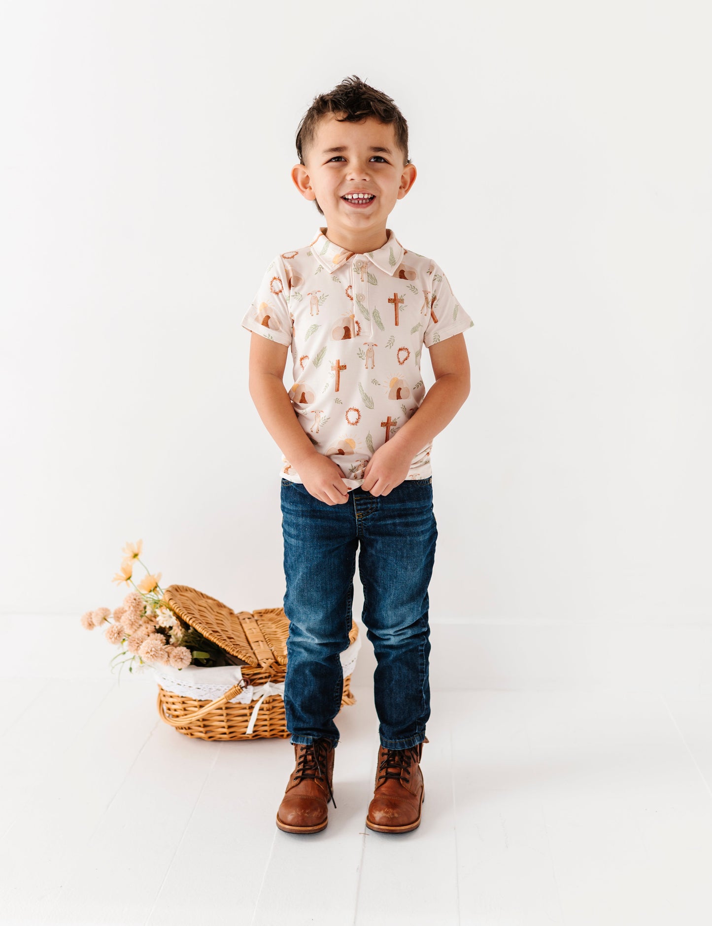 Child wearing a Easter patterned shirt and jeans standing next to a woven basket on a white background