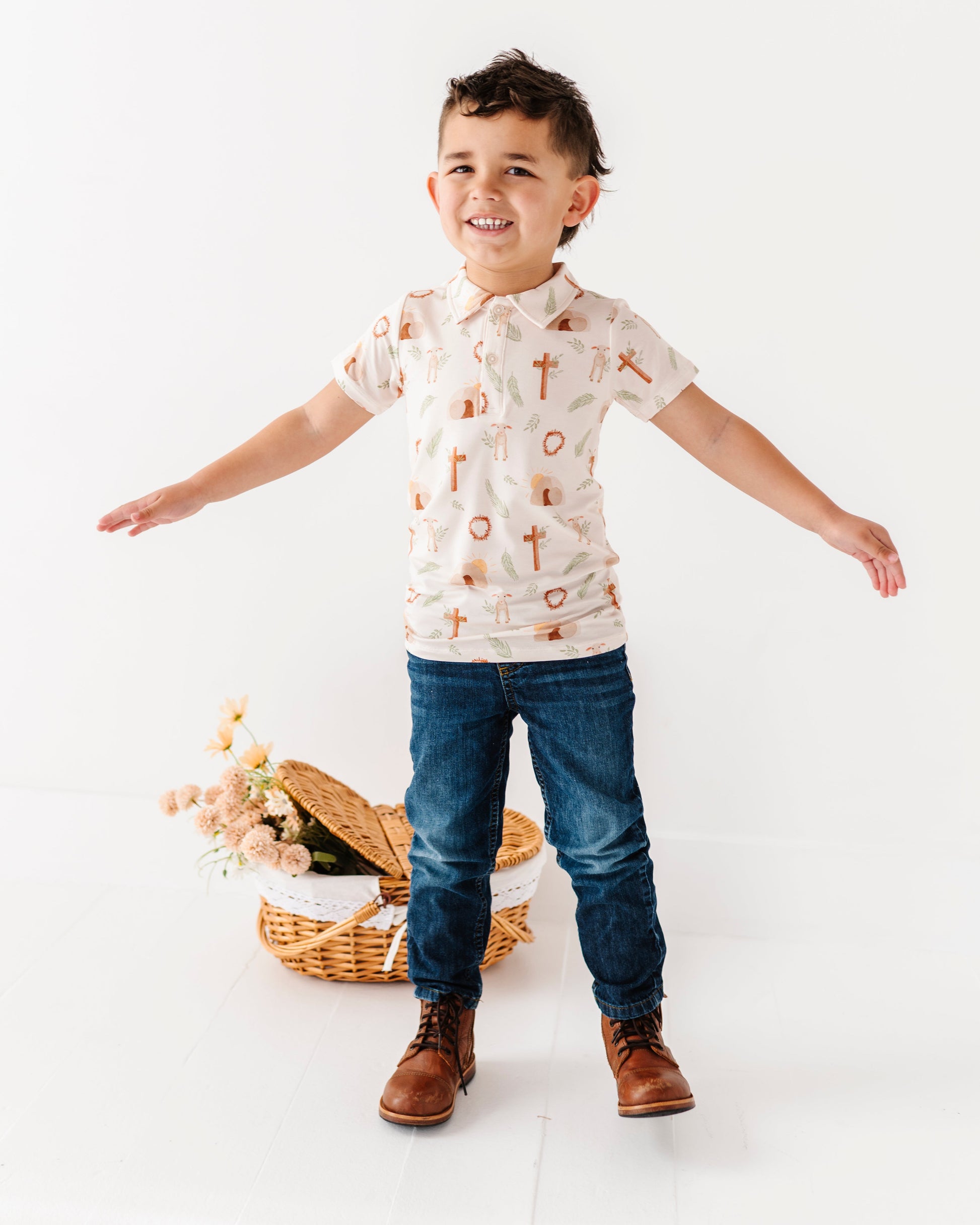 Child wearing an Easter shirt and jeans standing on a white background with a basket of flowers.
